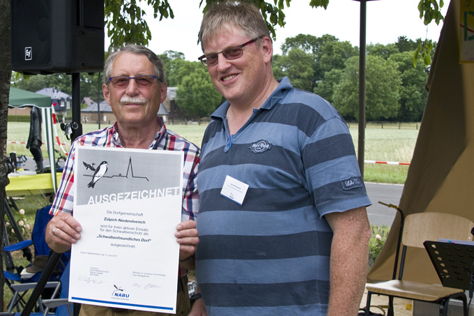 Heinz Hettner (li), Ortsvorsteher aus Zülpich-Niederelvenich, erhält beim Dorffest im Juni 2017 von Uwe Wedegärtner die Auszeichnung Schwalbenfreundliches Dorf 